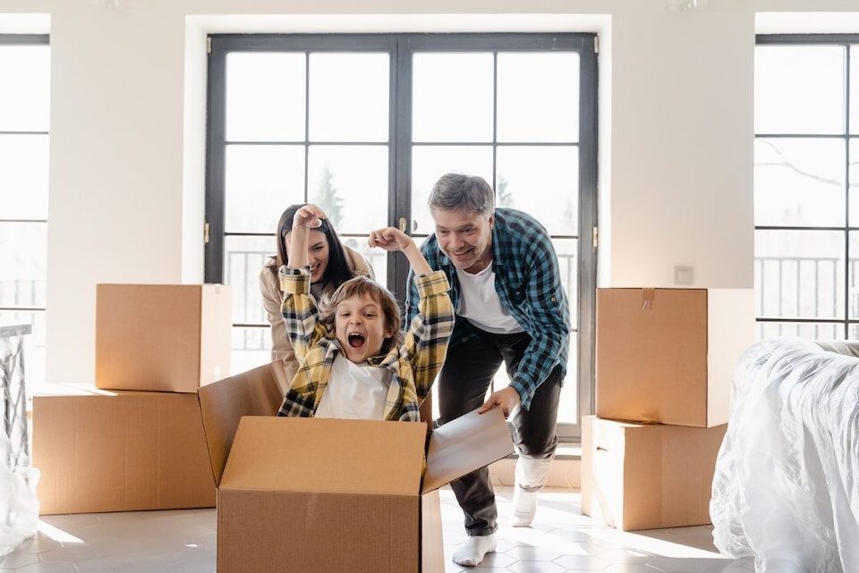parents pushing a box with their kid in it across a room