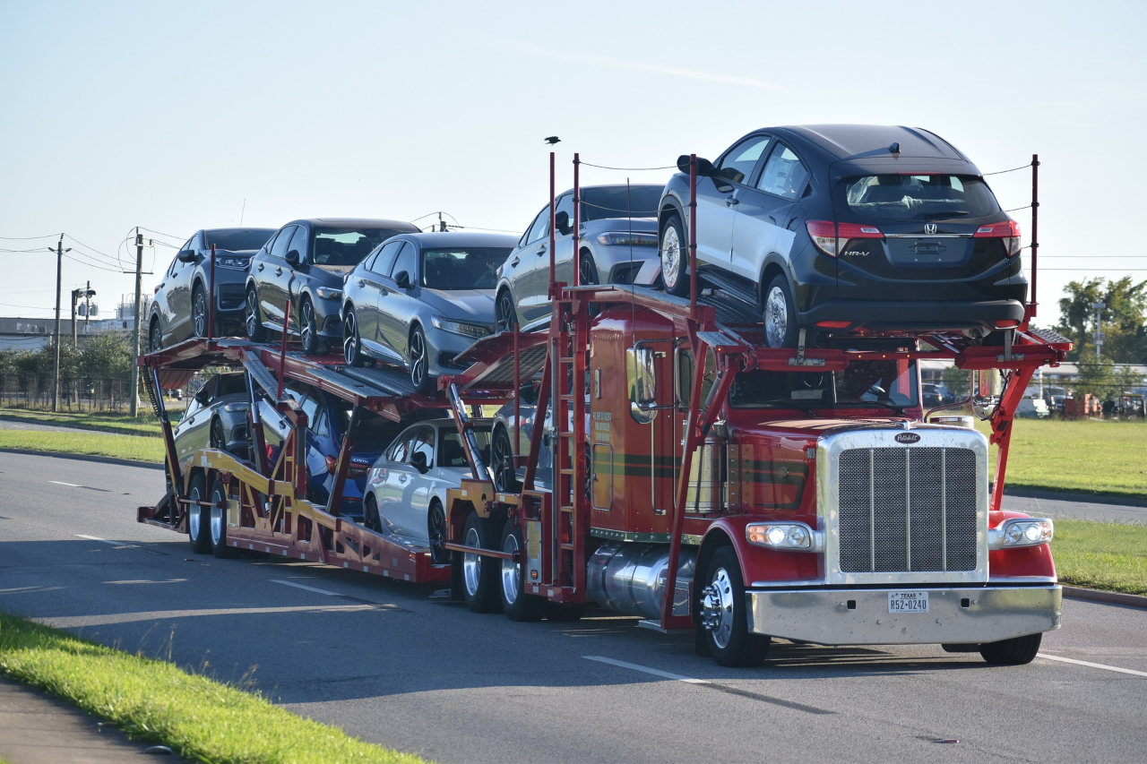 A red auto transport truck loaded with a variety of cars, including sedans and SUVs.
